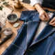 Manos trabajando en la confección de una chaqueta azul sobre una mesa de sastrería